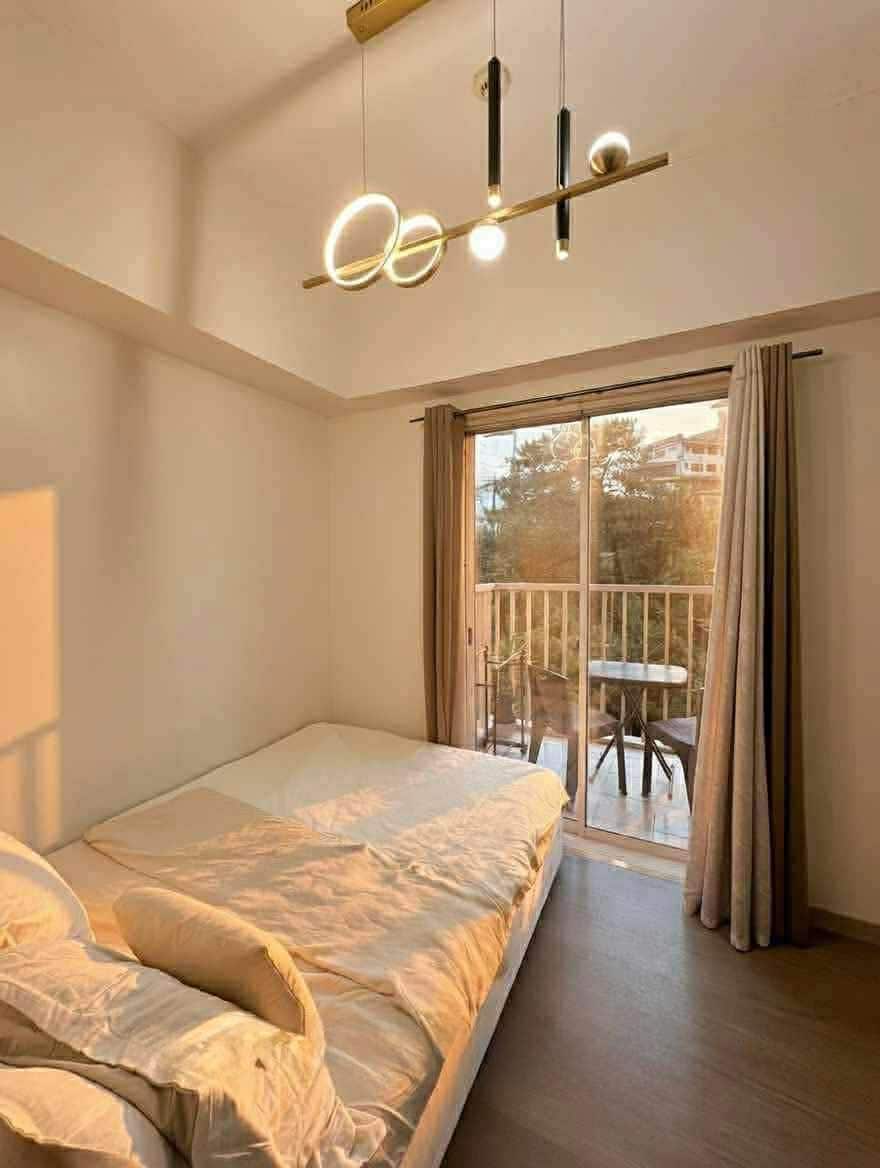 Double bed under a ring pendant light beside the balcony doors